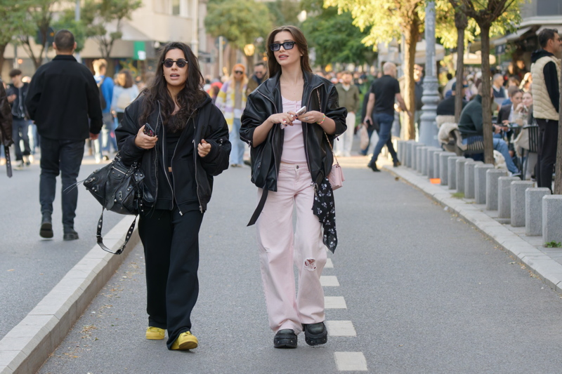 24 - Two women walking down a city street wearing casual streetwear, including black leather jackets and sunglasses